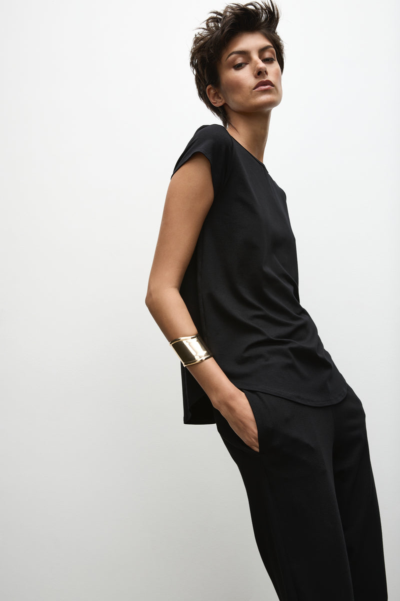 A person wearing a black high-neck, short-sleeved top with a curved hemline, paired with dark pants.