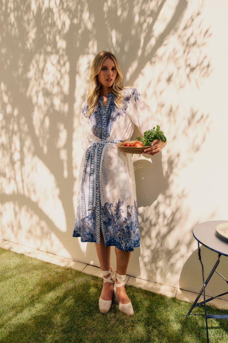 Woman in a blue and white dress holding a tray of vegetables against a white wall.