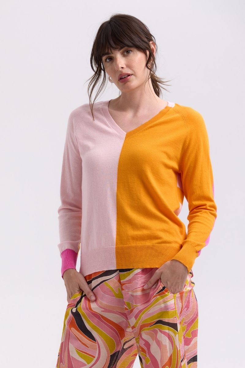 Woman wearing a colorful outfit with a pink and orange top and patterned pants on a white background