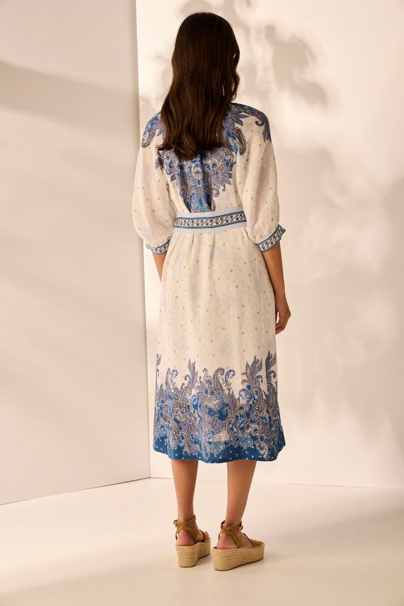 Back view Woman wearing a long, light-colored dress with blue floral patterns against a plain background