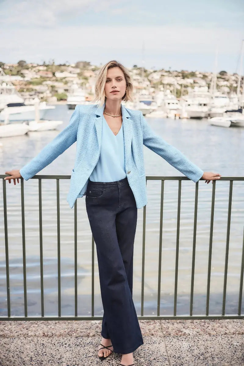Woman in light blue blazer and dark Blue Denim Goldie wide Leg Jeans By Joseph Ribkoff  standing by a waterfront with boats in the background
