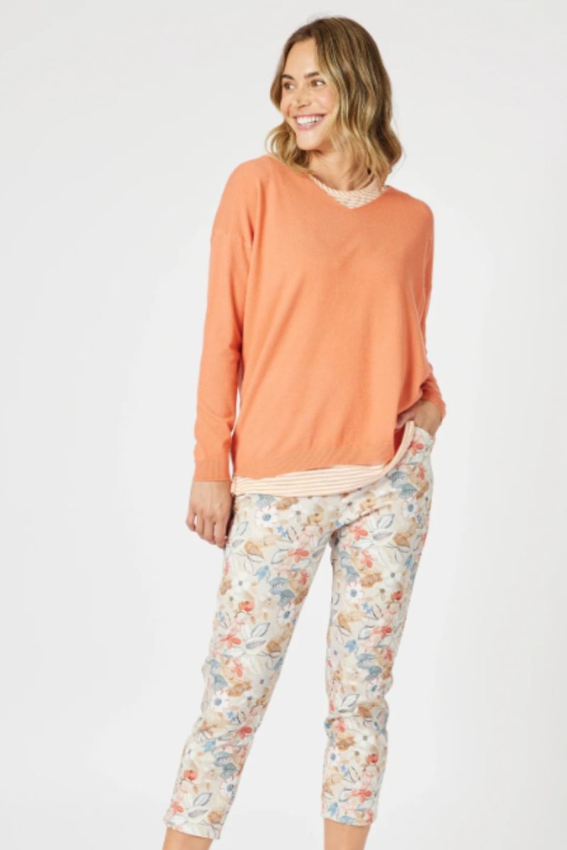 Woman wearing an orange long-sleeve top and floral leggings on a white background