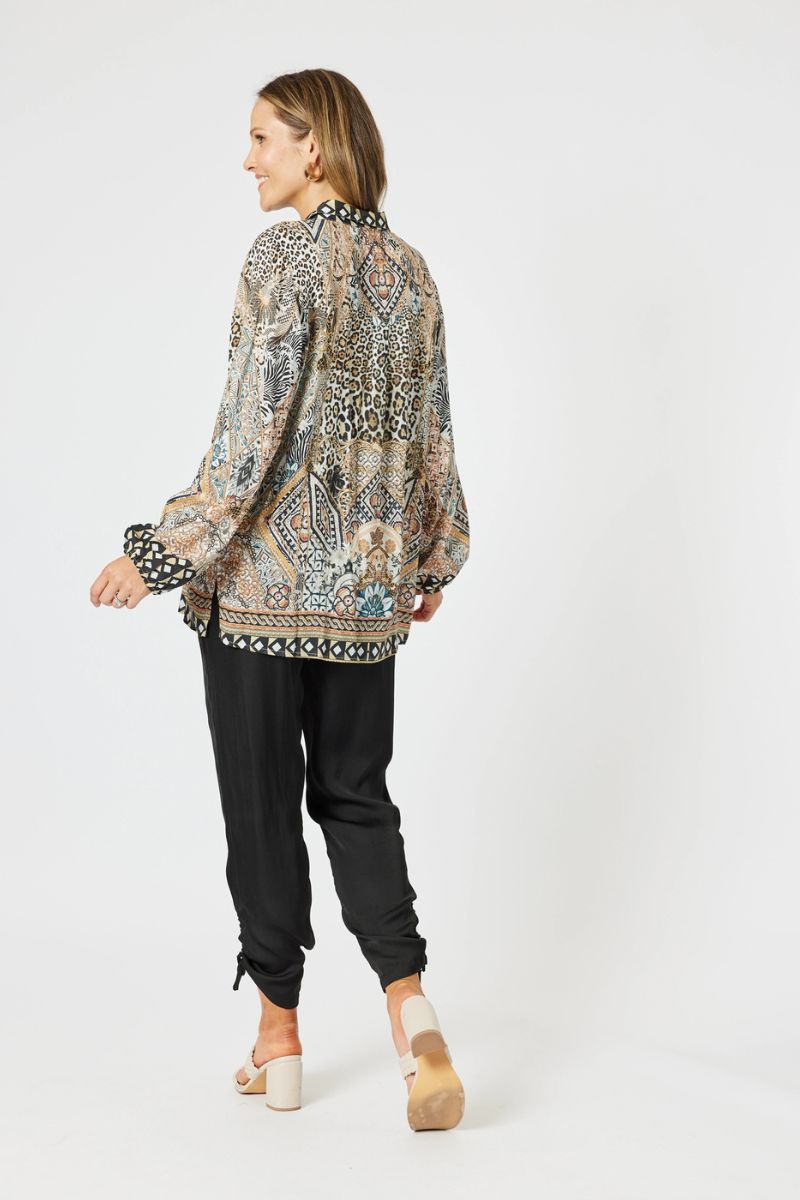 Woman wearing a patterned blouse and black pants on a white background