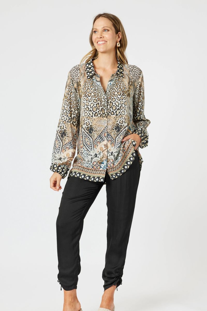 Woman wearing a patterned blouse and black pants on a white background