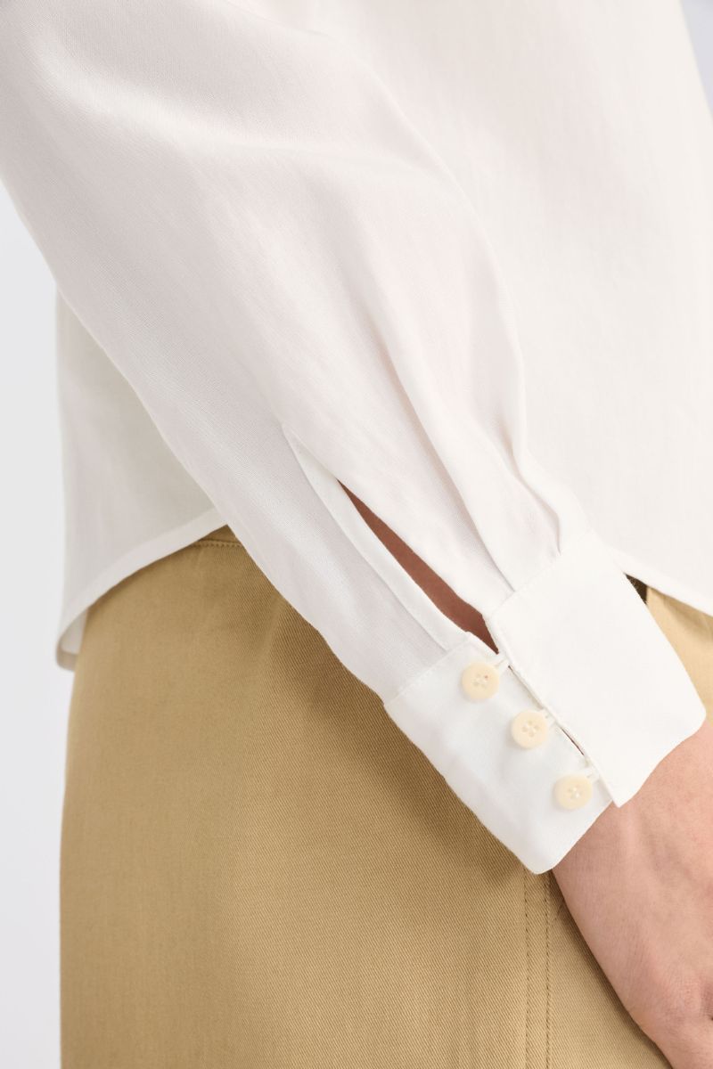 Close-up of a white shirt with rolled-up sleeves and beige pants on a light background