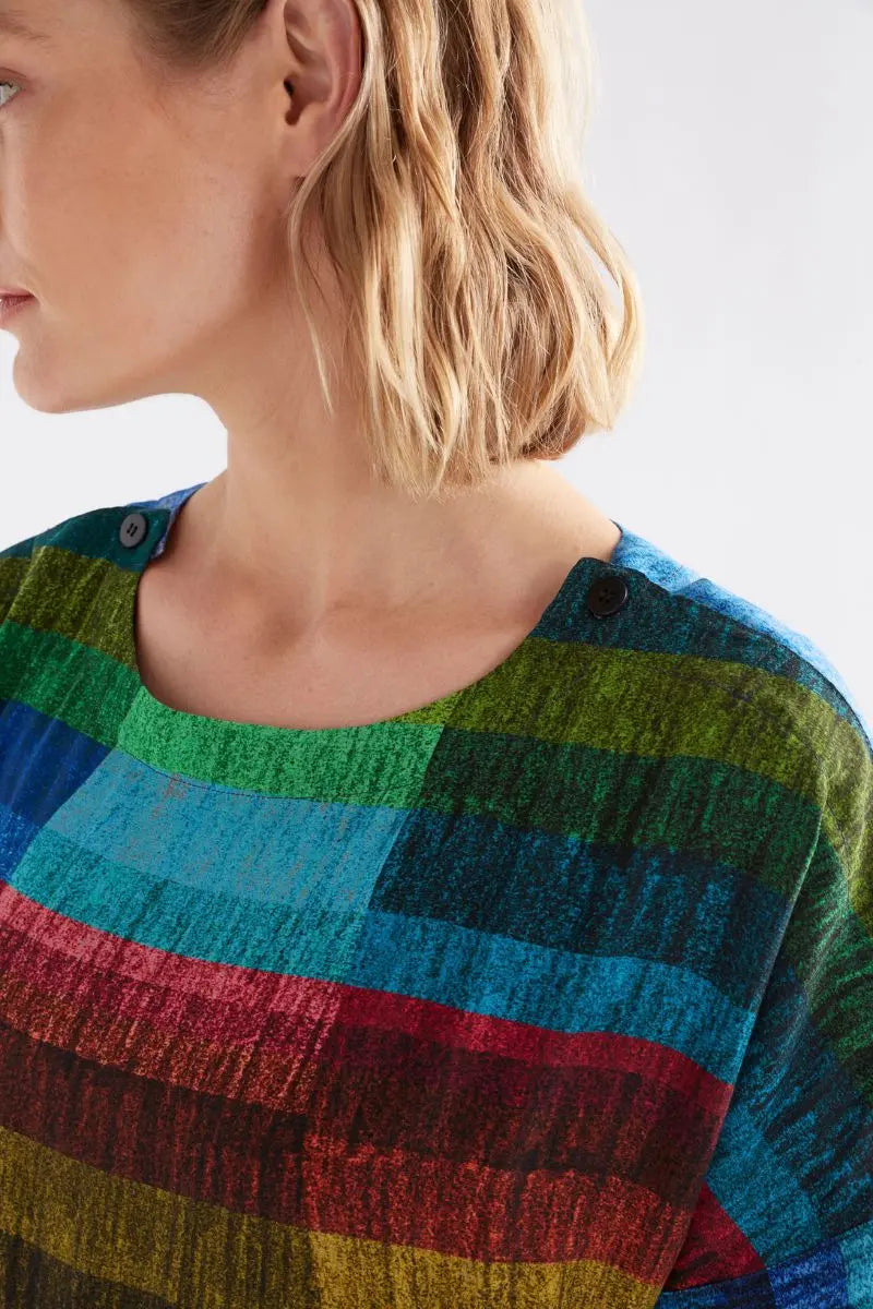 Close-up of a person wearing a colorful striped Sono top with a neutral background