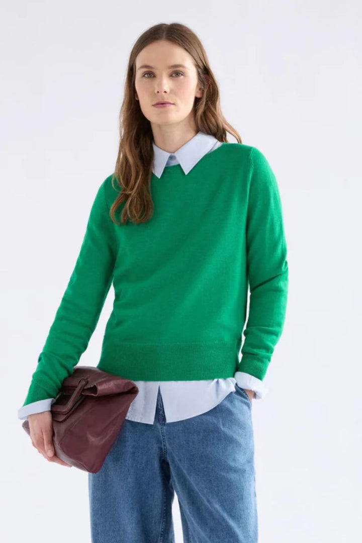 Woman wearing Elk the Label Allora Sweater in green with jeans on a white background