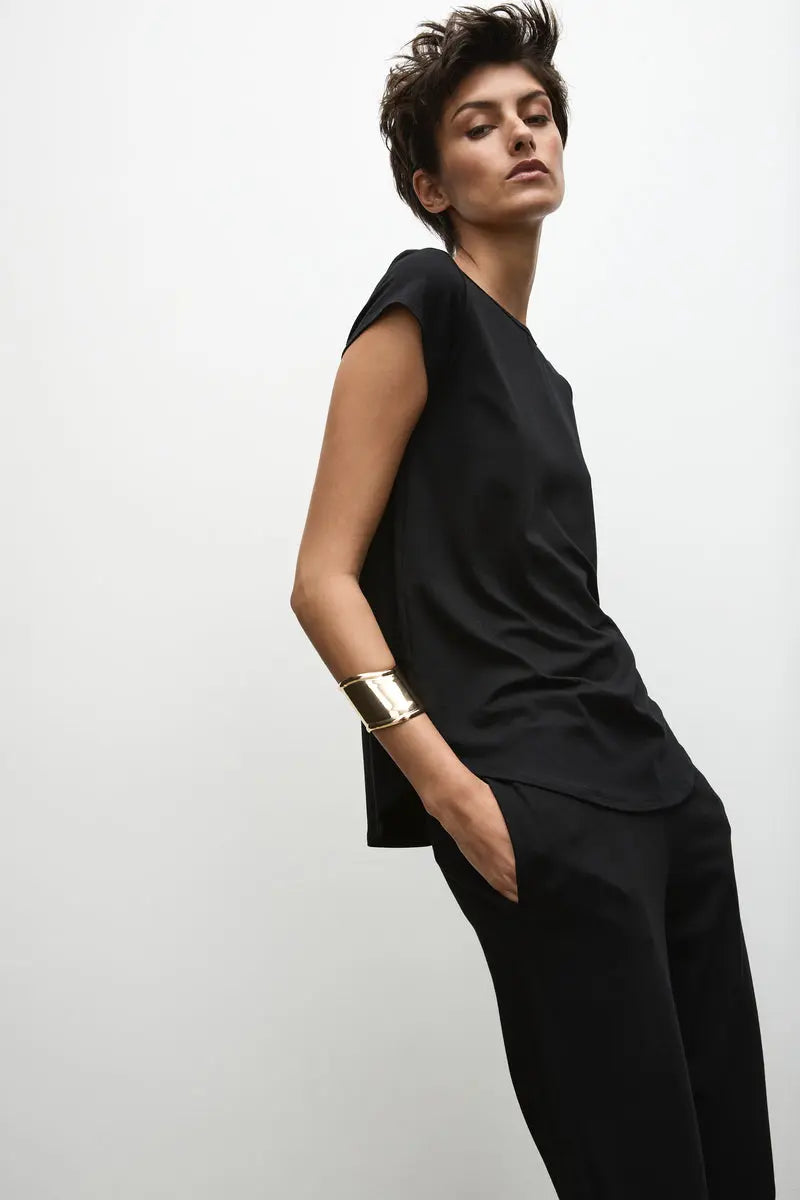 A person wearing a black high-neck, short-sleeved top with a curved hemline, paired with dark pants.