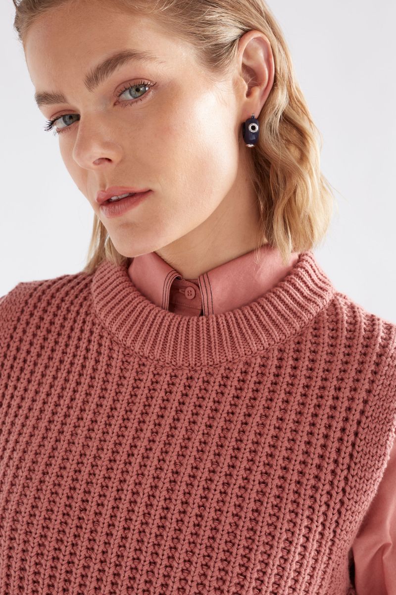 Person wearing a pink knitted sweater over a collared shirt with a plain background