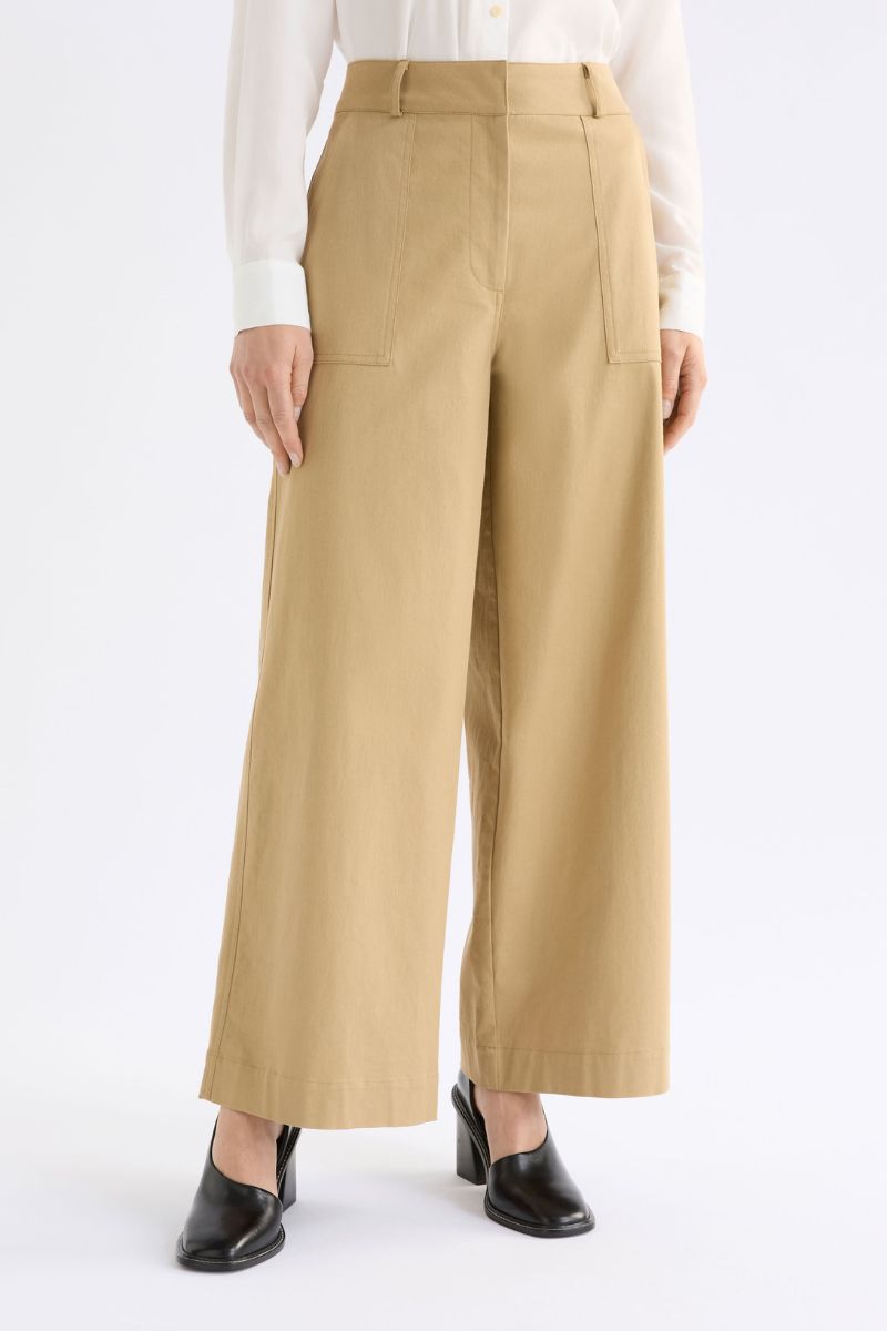 Beige wide-leg pants worn with a white shirt and black shoes on a white background