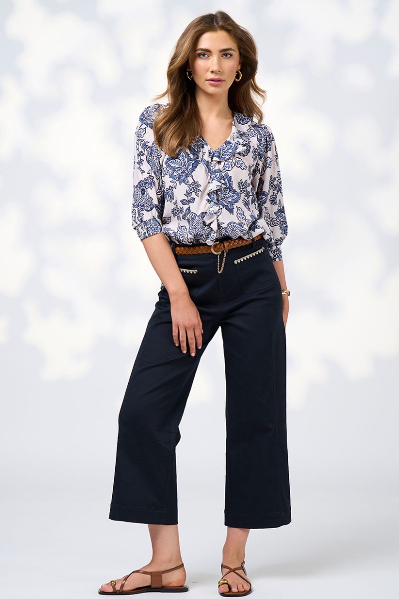 Woman wearing a blue floral blouse and dark pants on a white background