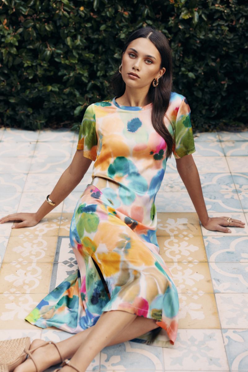 Woman wearing a colorful dress sitting on a patterned floor with greenery in the background