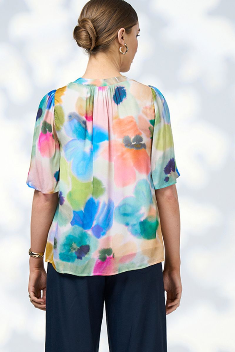 Back view of a woman wearing a colorful floral blouse against a light background