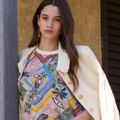Woman wearing the loobie's Story Ceylon top and Cream jacket leaning against a wall.