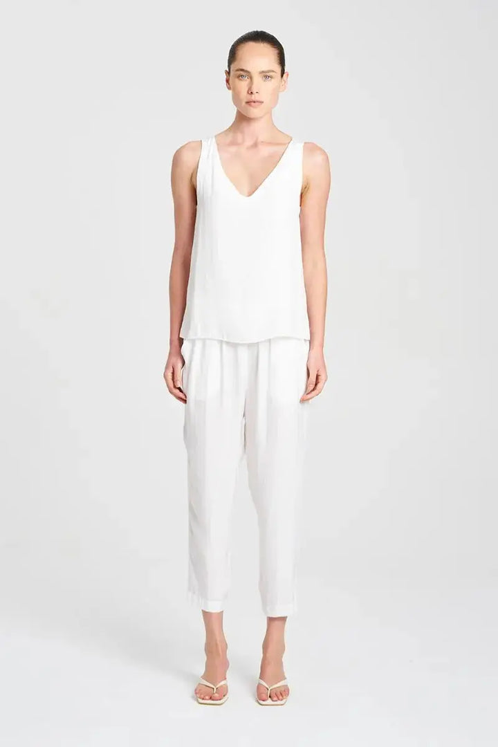 Woman wearing a white sleeveless top and pants on a light gray background