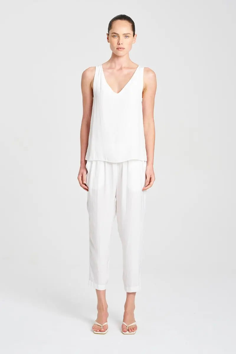 Woman wearing a white sleeveless top and pants on a light gray background