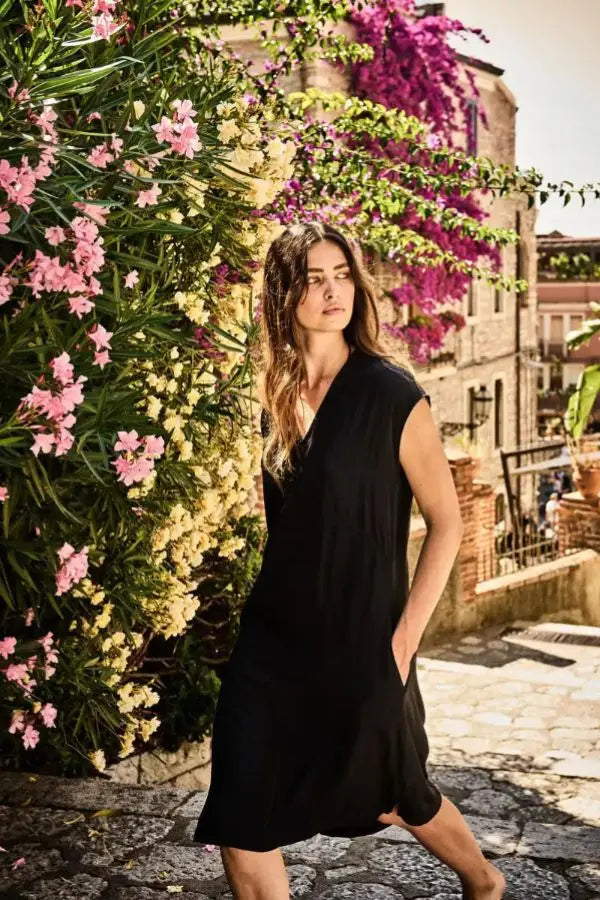 Woman in a black mela Purdie Dress  standing in front of a building with flowers