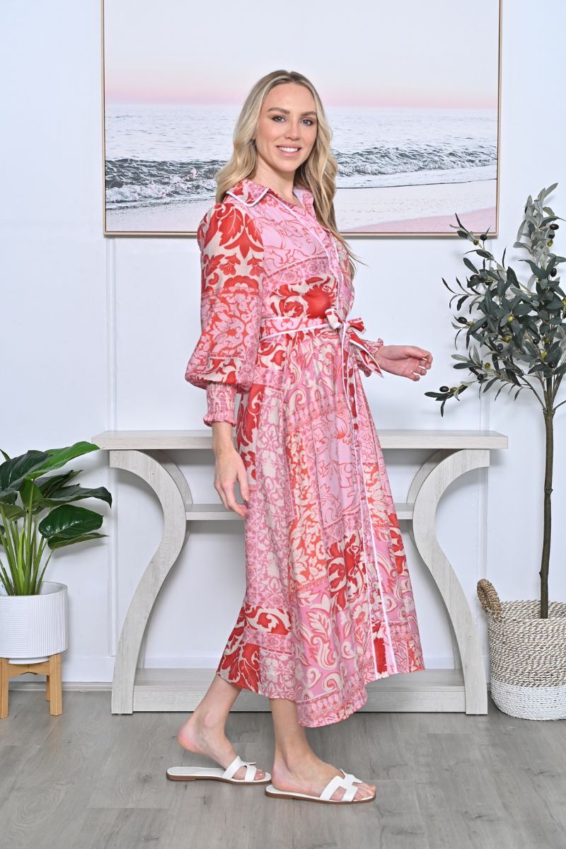 Woman wearing a pink floral dress standing in a room with plants and a decorative wall piece.