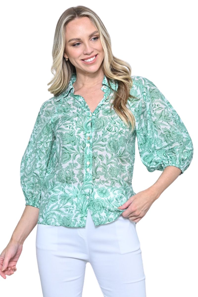 Woman wearing a green floral blouse with white pants on a white background