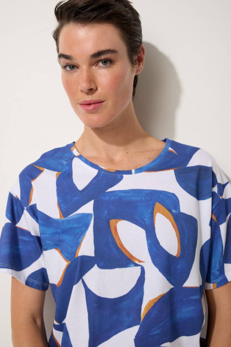 Woman wearing a blue, orange and white patterned tee shirt against a plain background Marco polo reflections tee YTMP7501