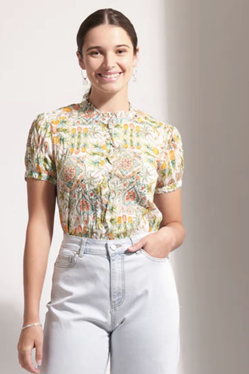 Woman wearing a floral blouse and light jeans against a plain background