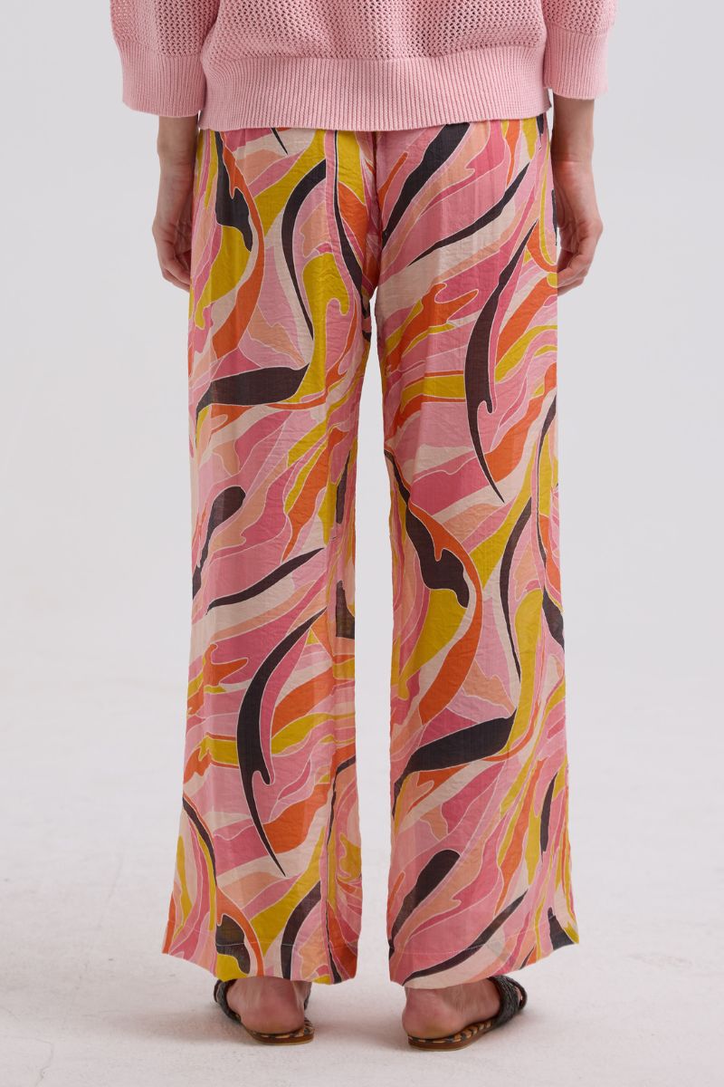 Person wearing a pink sweater and colorful patterned pants on a white background