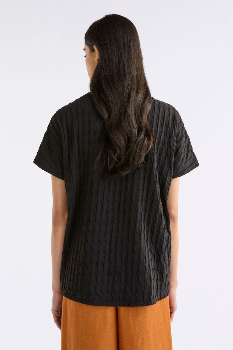 back view of person wearing a black textured shirt and orange pants on a white background