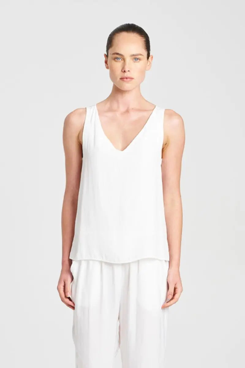 Woman wearing a white sleeveless top and pants on a light gray background