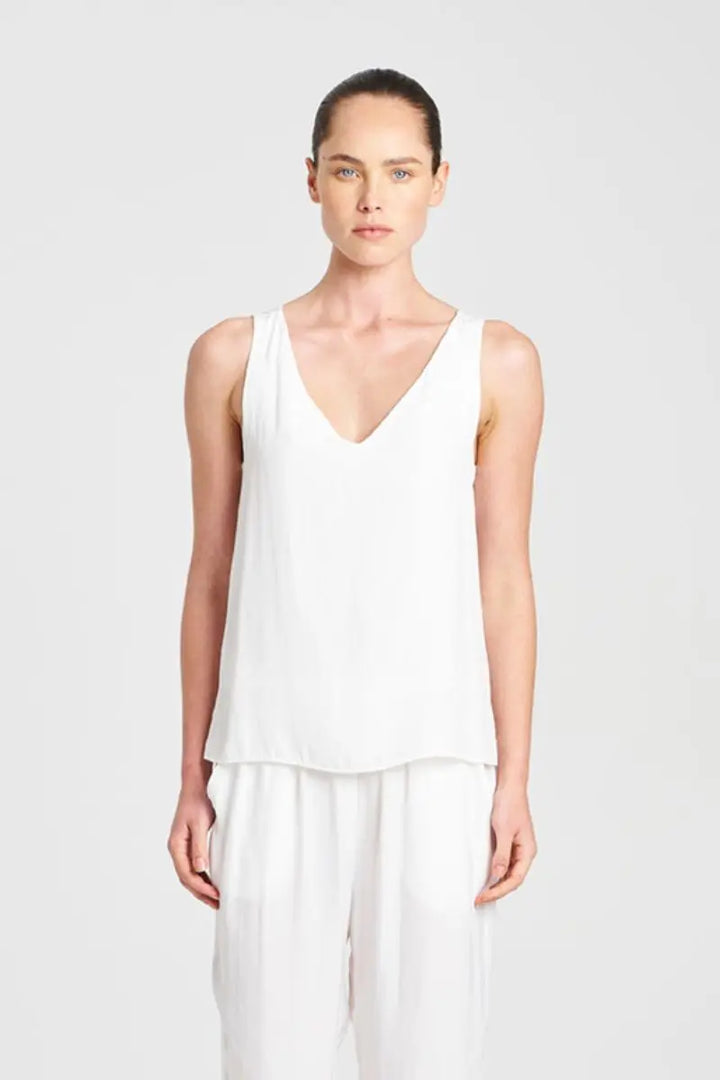 Woman wearing a white sleeveless top and pants on a light gray background