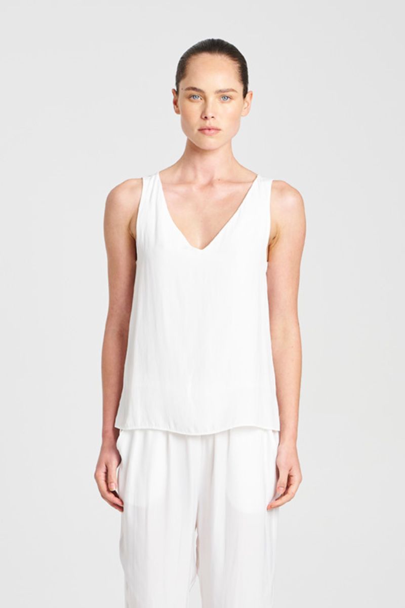 Woman wearing a white sleeveless top and pants on a light gray background