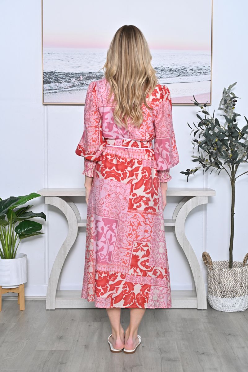 Woman in a pink floral dress standing in a room with plants and a painting on the wall.