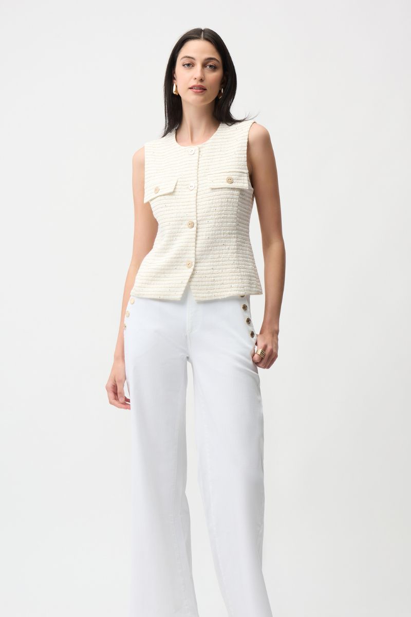 Woman wearing a cream-colored sleeveless jacket and white pants on a light gray background