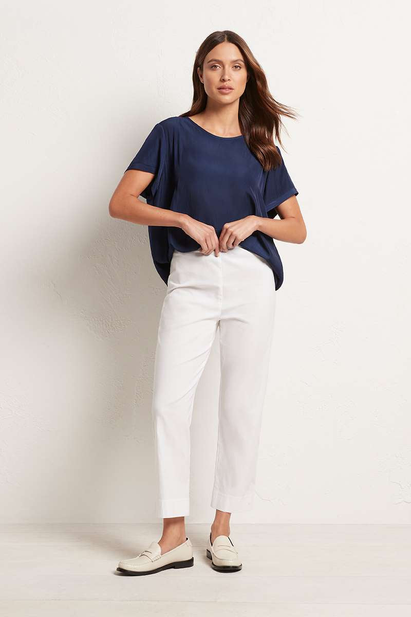 A woman wearing a navy blue top and Mela Purdie Cropped Pant F65 1348 in white against a plain background