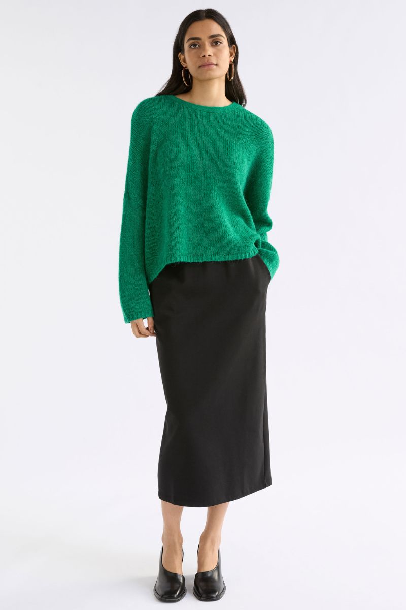 Woman wearing a green sweater and black skirt on a white background