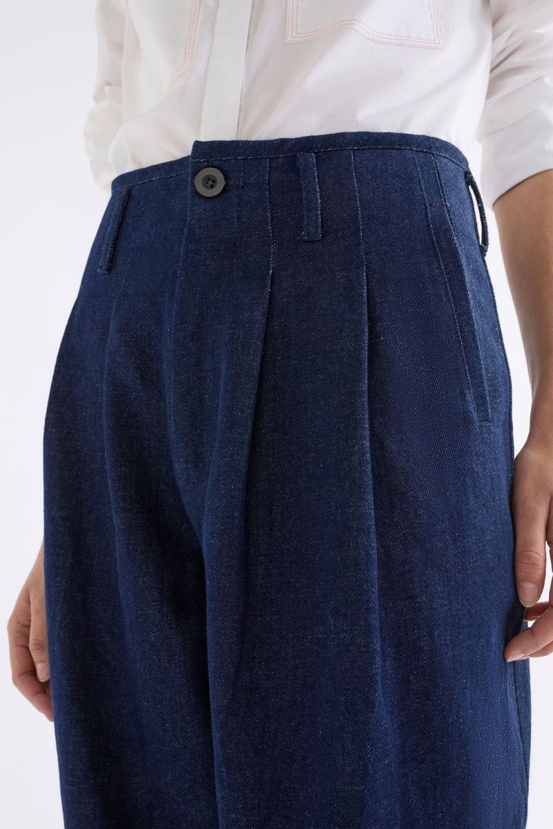 Navy blue pleated pants worn with a white shirt on a light background