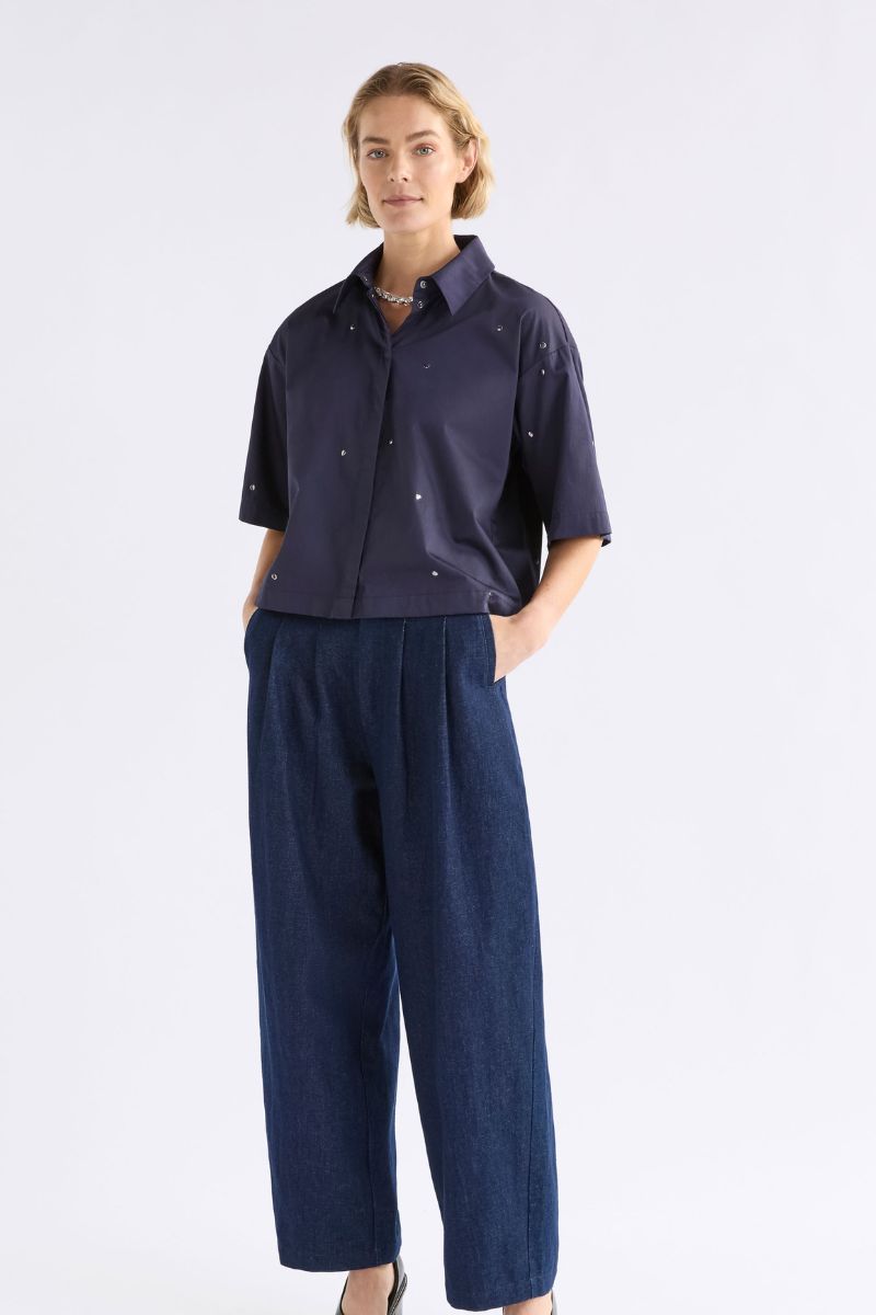 Woman wearing a navy blue outfit with a shirt and wide-leg pants on a white background