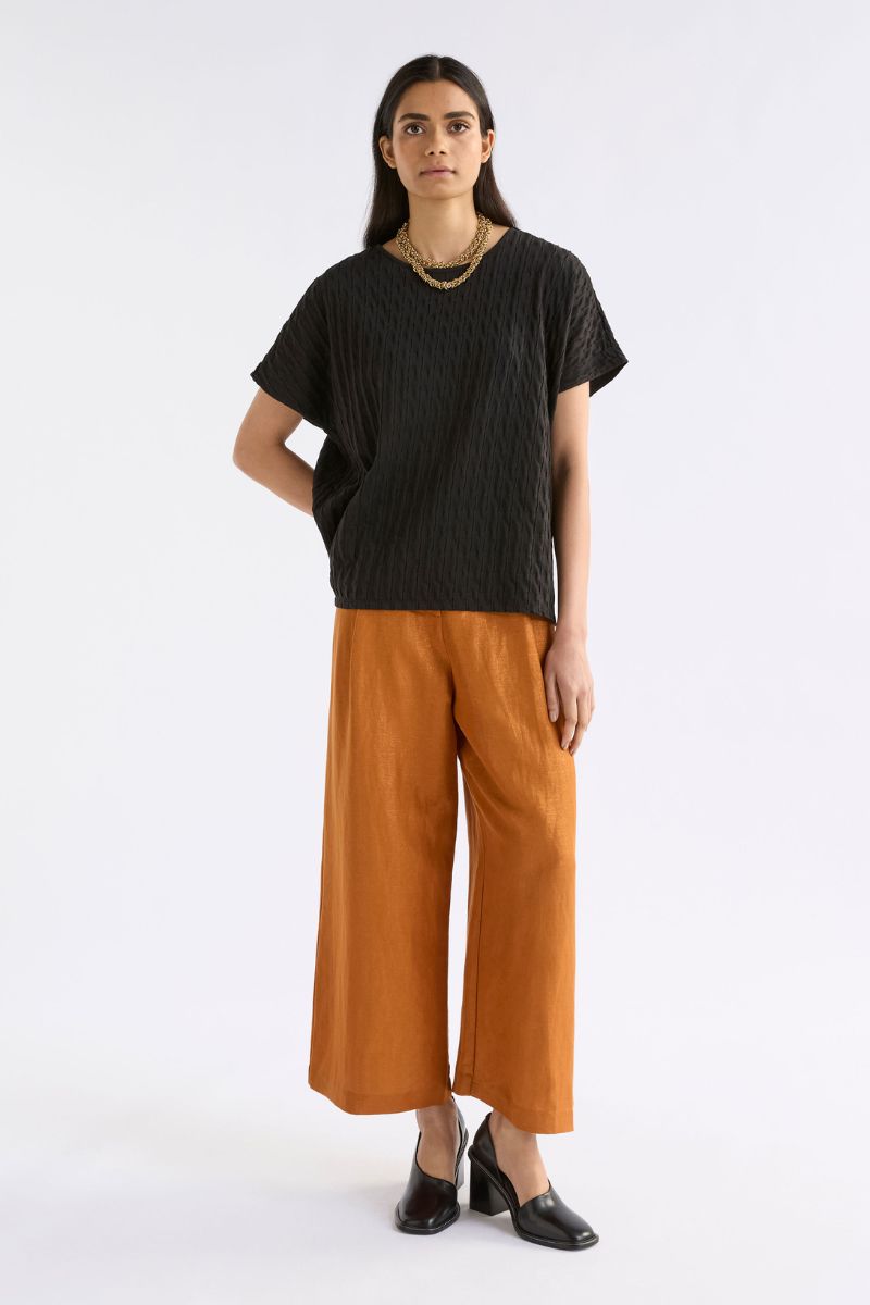 Woman wearing a black top and orange pants on a white background
