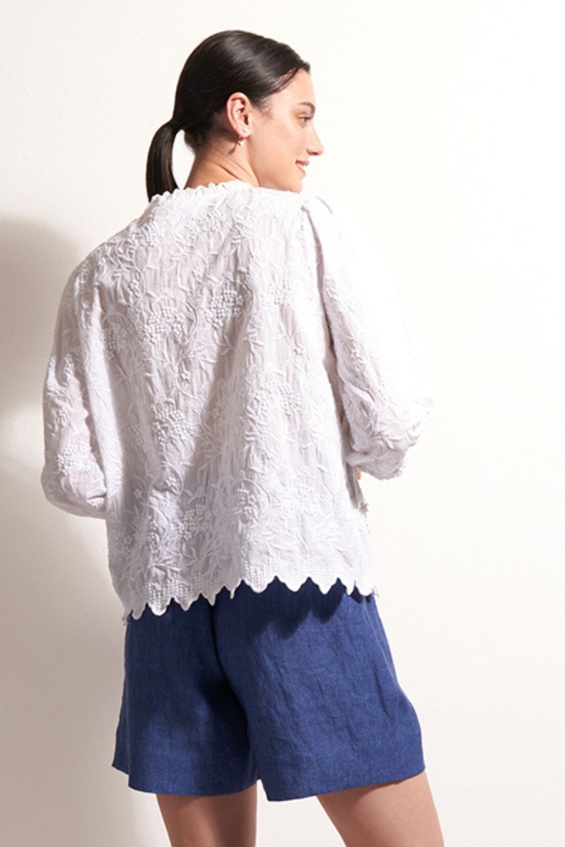 Woman wearing a white textured blouse and blue shorts on a plain background