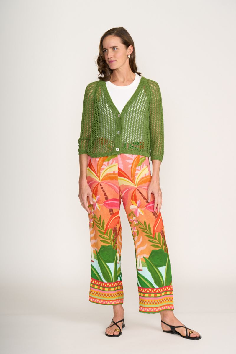 Woman wearing a green cardigan and colorful tropical print pants on a white background