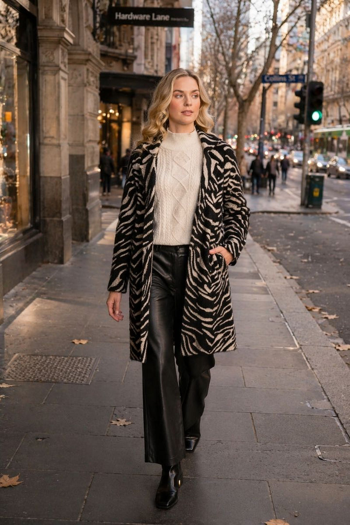 Women walking along a busy city street wearing black pants cable knit cream jumper and a zebra print coat by foil clothing called the lash queen coat.