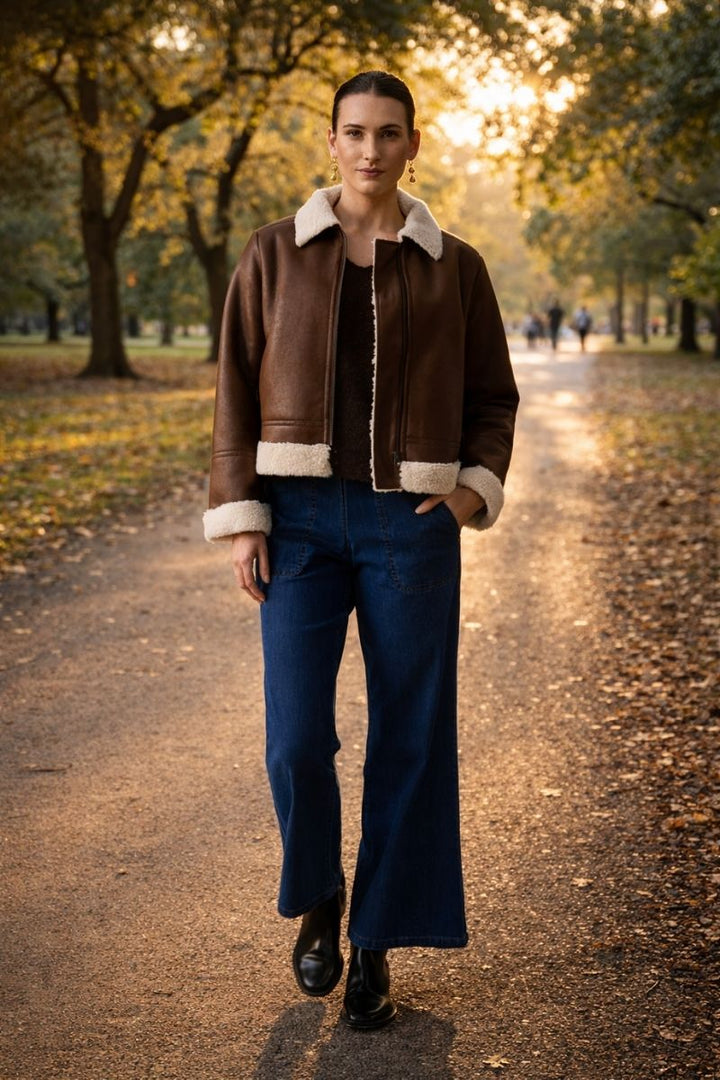 Woman wearing jeans and foil clothings the flying high jacket in coffee with cream collar and edging in a flight jacket style walking in a park