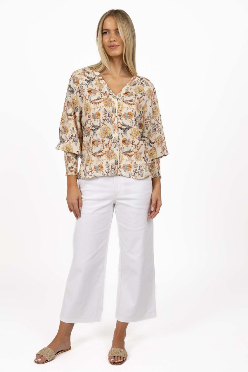 Woman wearing a floral blouse and white pants on a white background