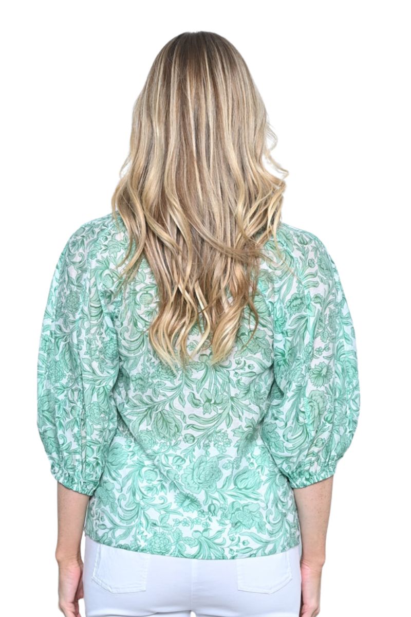 back view Woman wearing a light green floral blouse with white pants on a white background