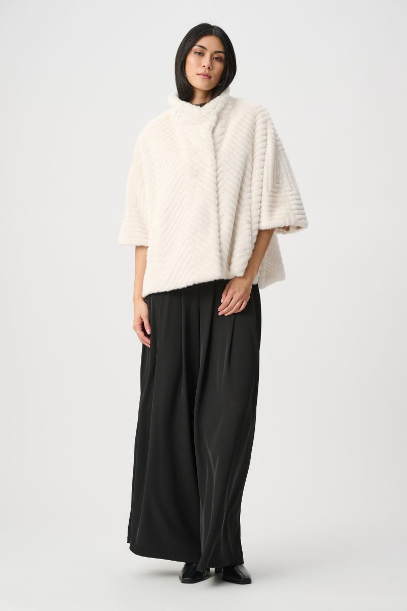Woman wearing Joseph Ribkoff cream chevron faux fur cape jacket with contrast black wide leg pants