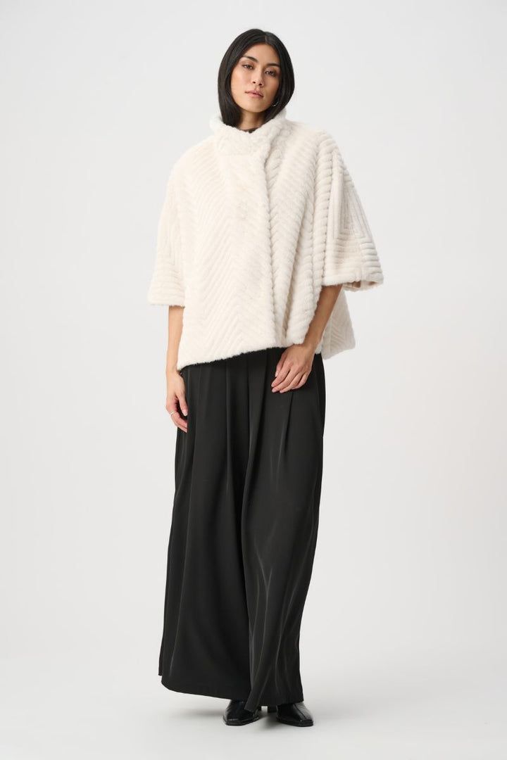Woman wearing Joseph Ribkoff cream chevron faux fur cape jacket with contrast black wide leg pants