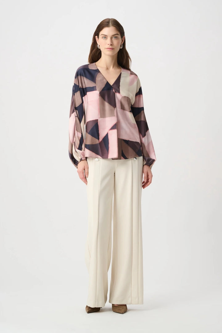 Joseph Ribkoff 264197 geometric print recycled satin top styled with cream wide-leg pants, full-length front view