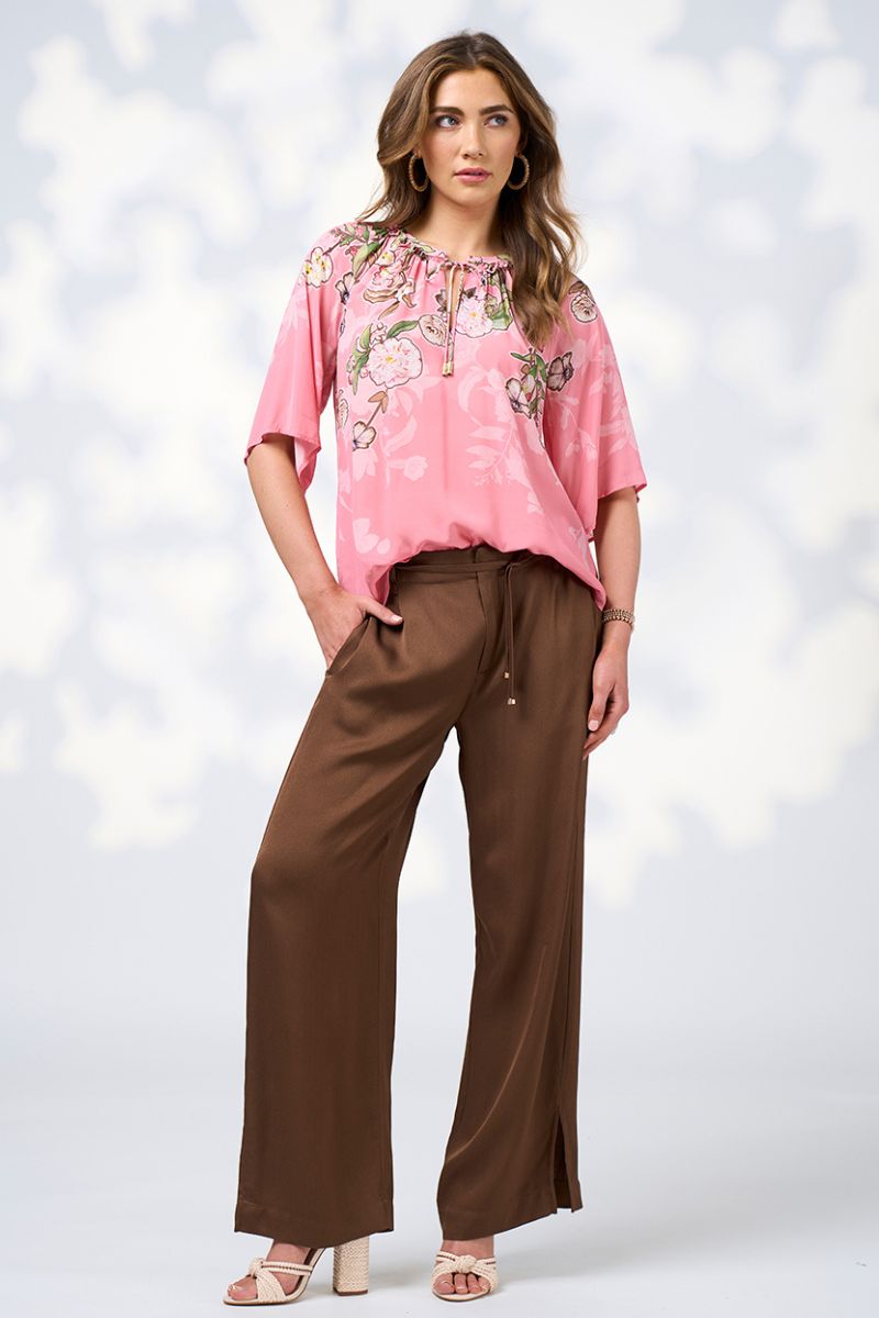 Woman wearing a pink floral blouse and brown pants against a white background
