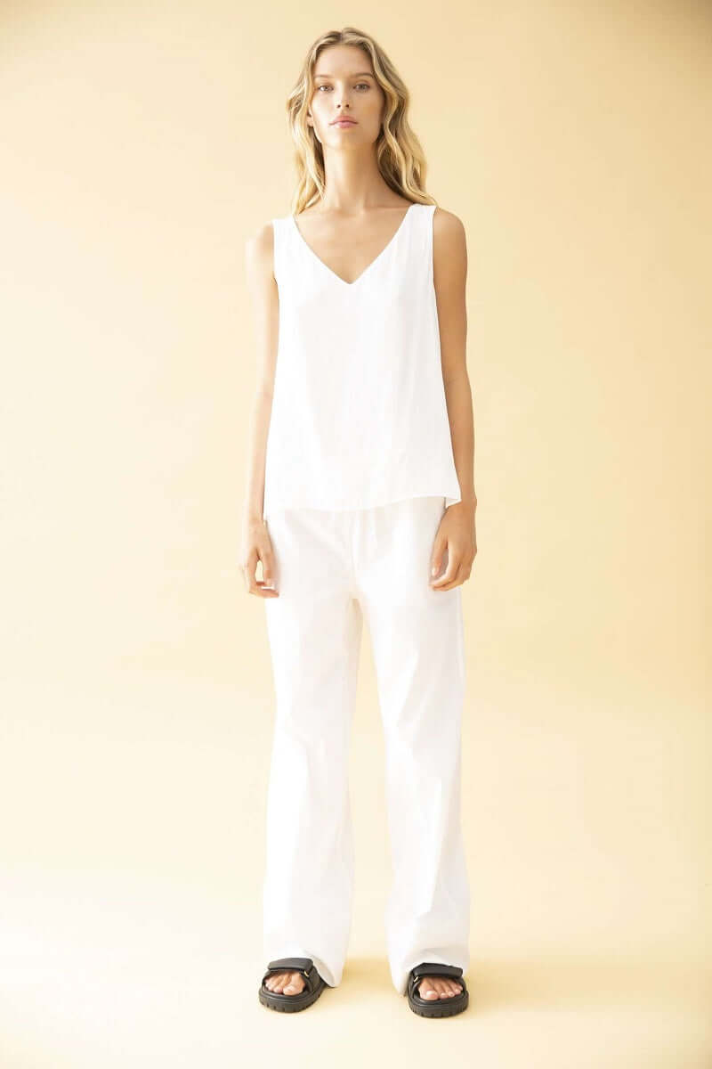 Woman wearing a White Audrey shape reference by Mela Purdie with white trousers and black sandals, front view. This listing is for Safari Python.
