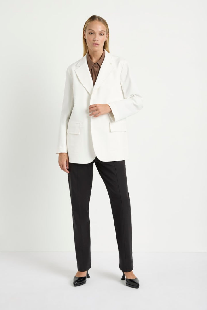 Woman wearing Stretch Blazer in Ivory by Mela Purdie F414 4129, front view with a brown shirt and black trousers.