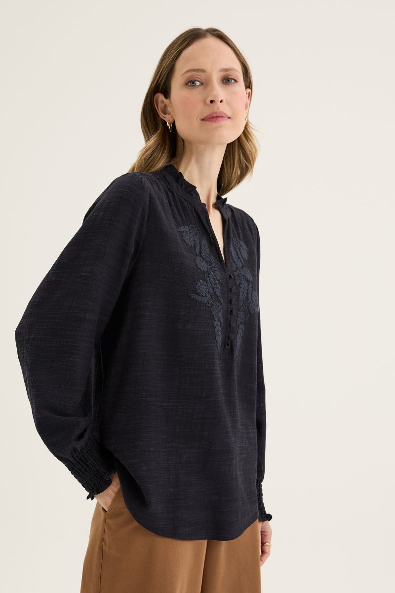 Woman wearing a dark blue blouse with floral embroidery on a light background